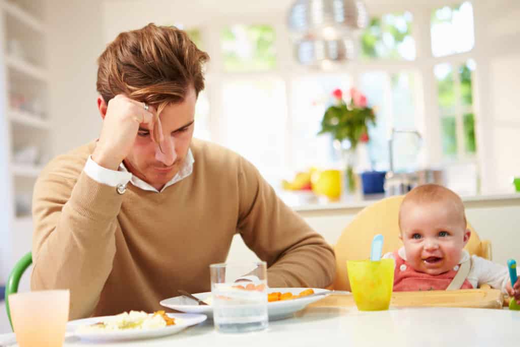 Father suffering from Paternal Postnatal Depression sitting at a table with his baby.